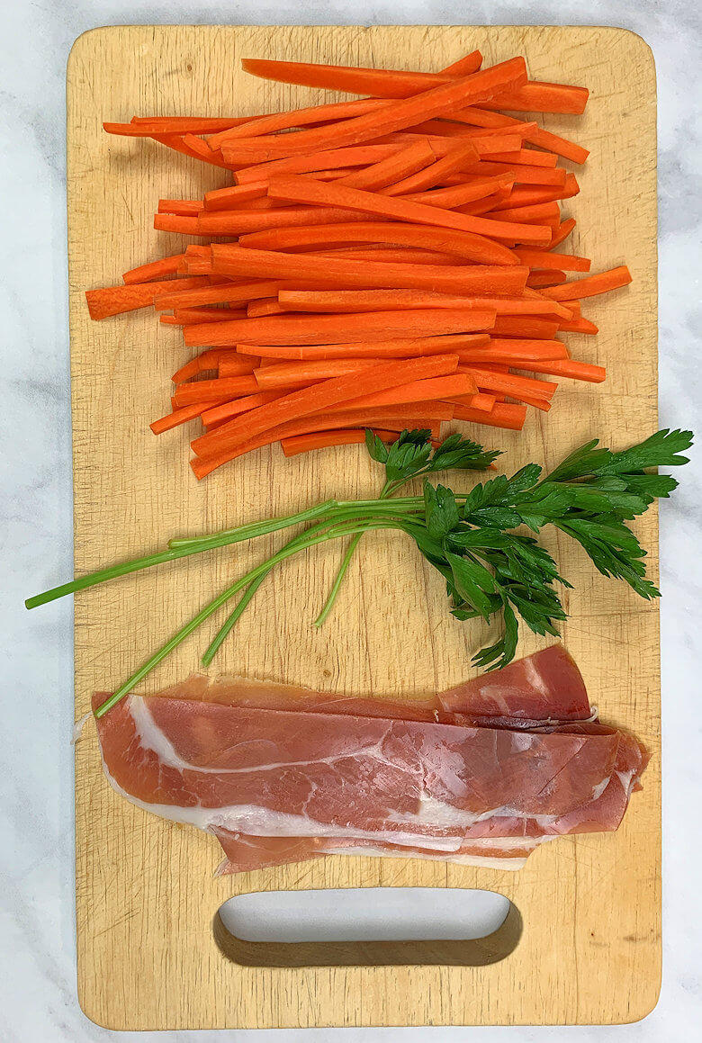 Wooden plank with carrot sticks, parsley and strips of Prosciutto ham