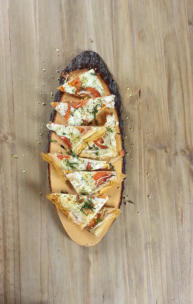 Picture of a cut Mediterranean Phyllo Pizza Caprese on a board