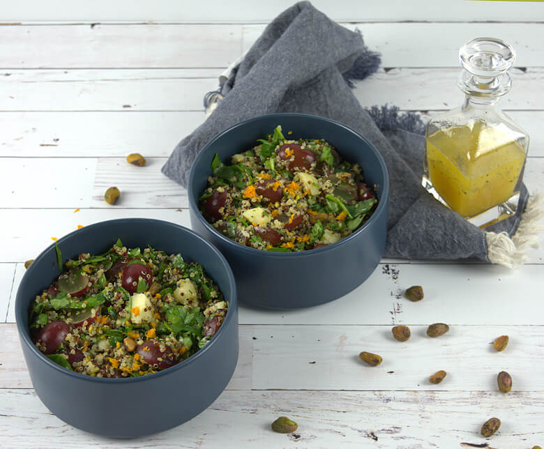 Two bowls of quinoa salad with grapes and dressing