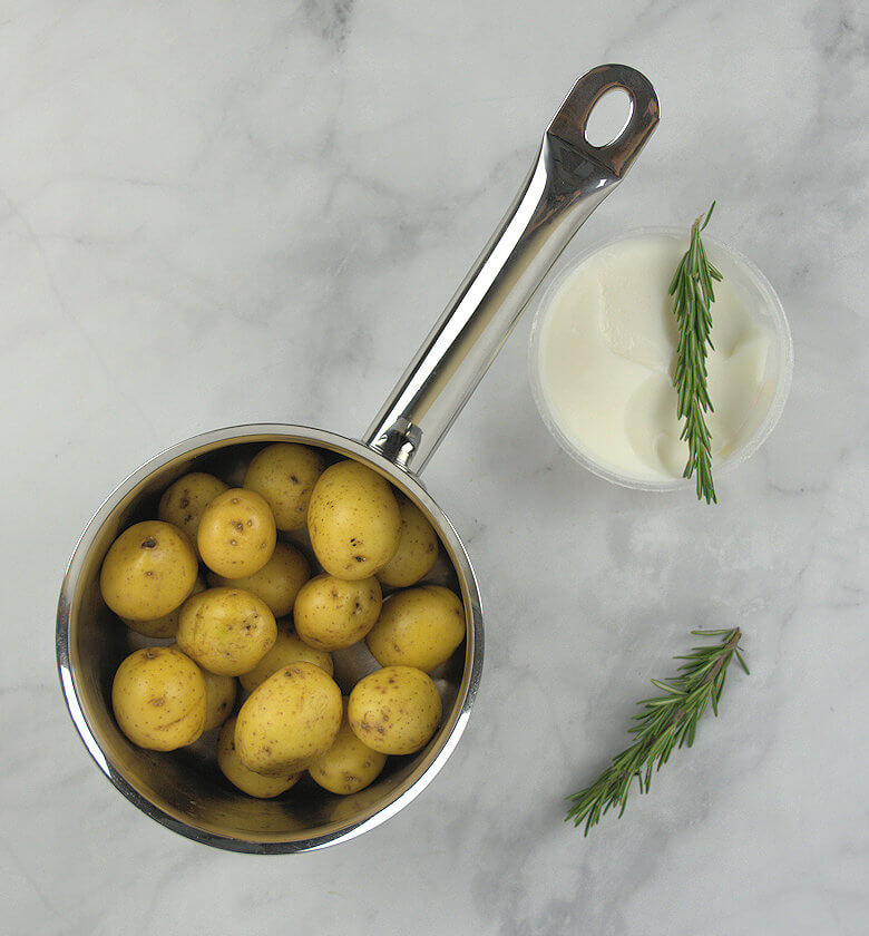 Picture of small potatoes in a pan with duck fat in tub and rosemary